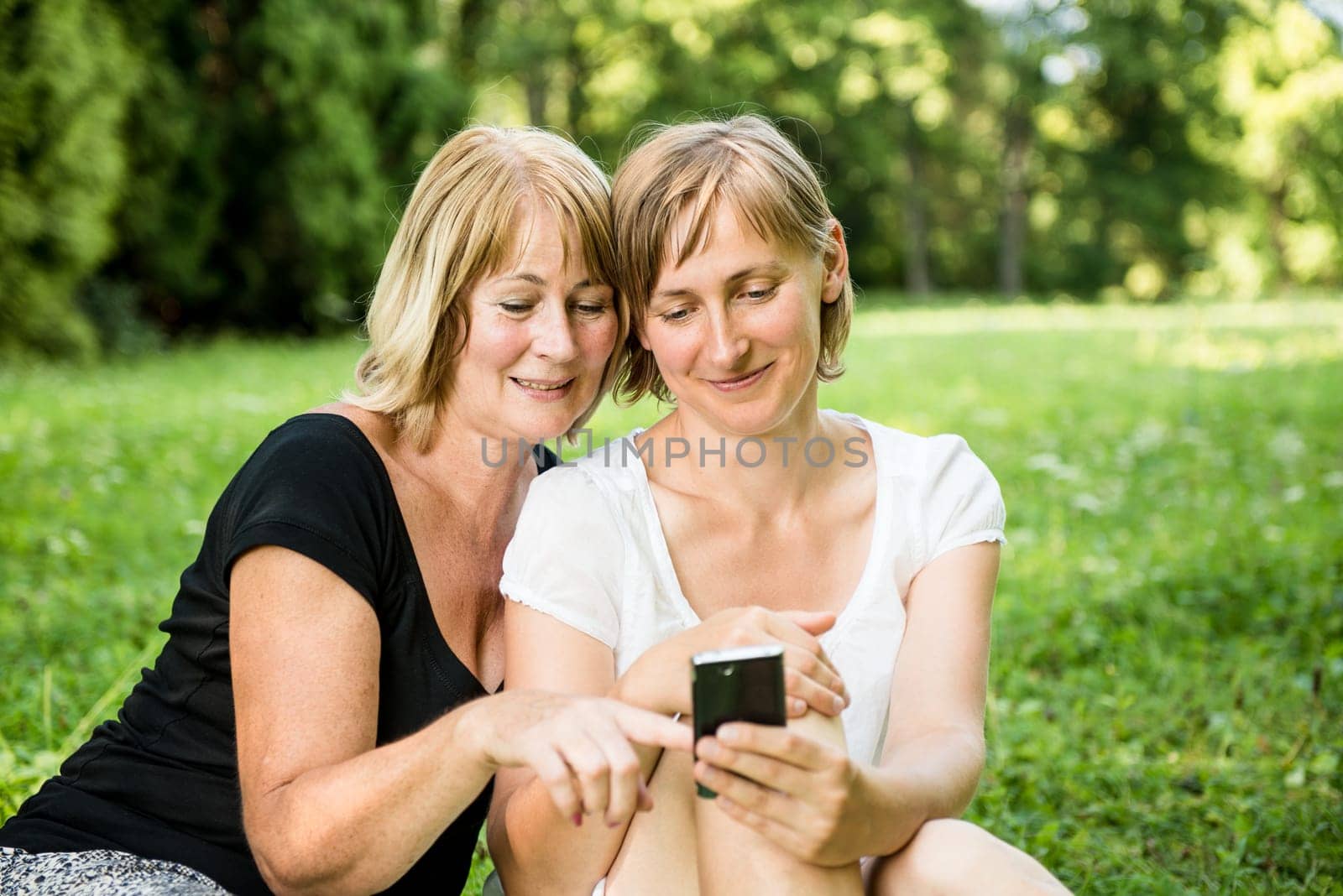 Senior mother showing on mobile phone to her adult child - outdoor in nature
