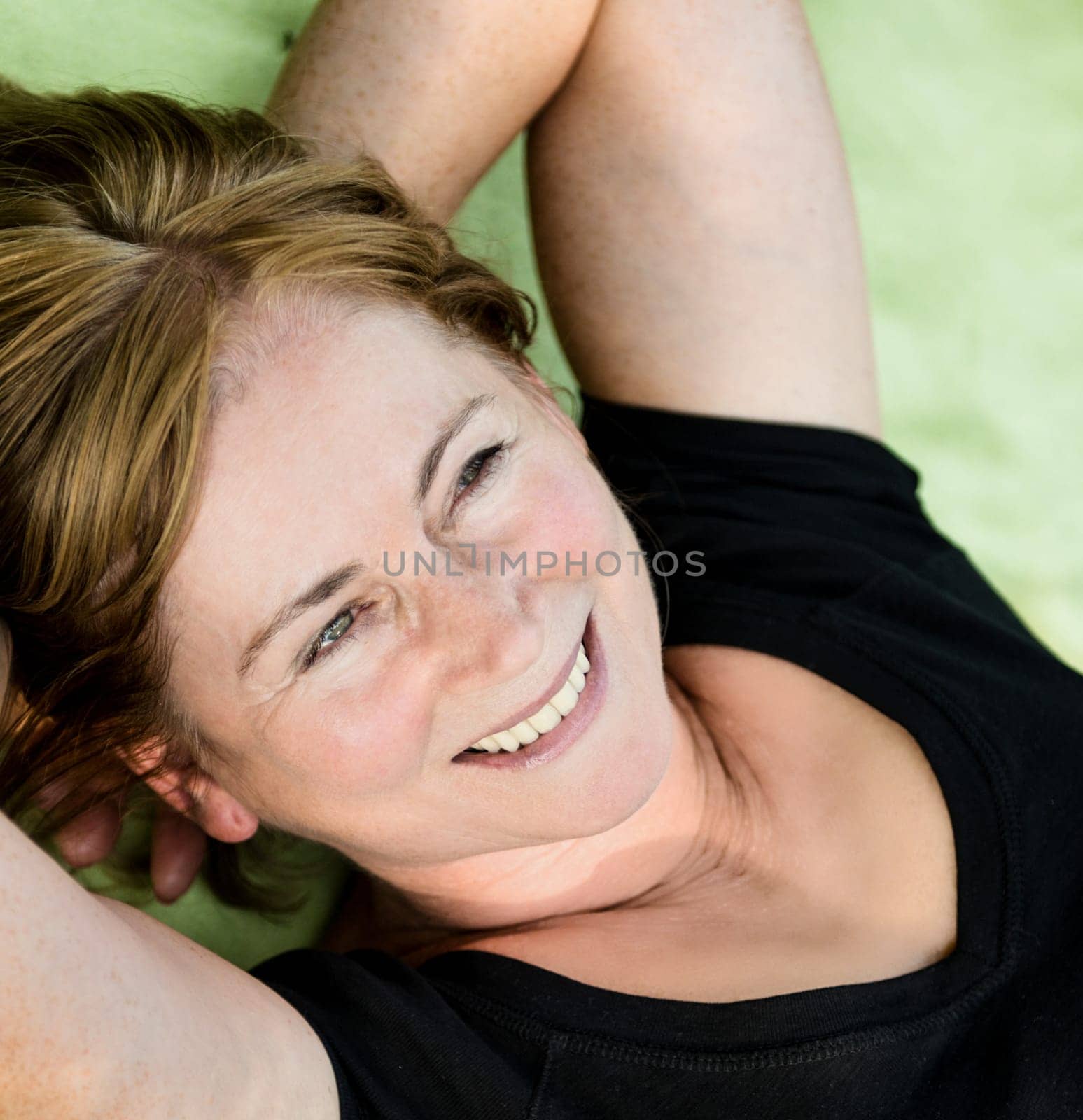 Smiling attractive senior woman lying outdoor on rug