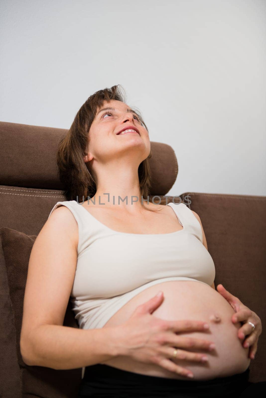 Portrait of happy pregnant woman holding belly sitting on sofa at home