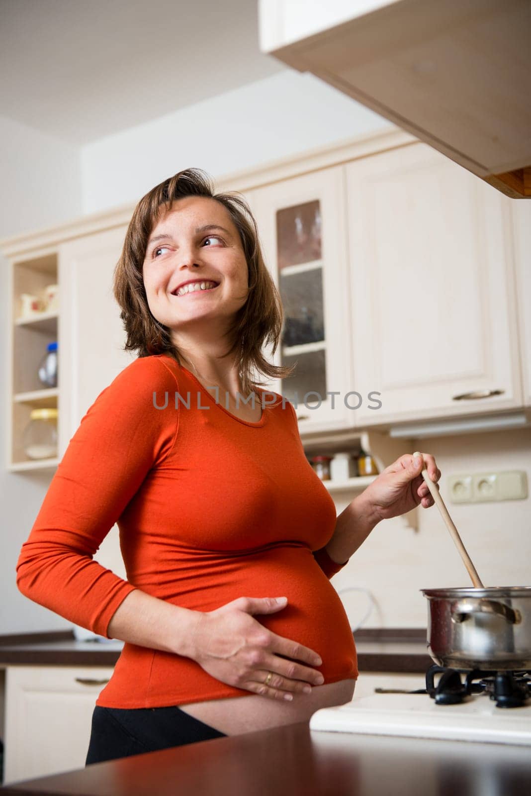 Lifestyle portrait of smiling pregnant woman cooking in kitchen, looking away