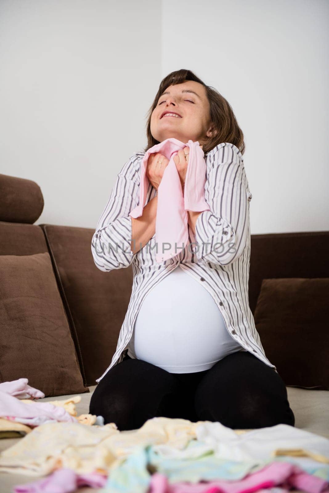Pregnancy - woman enjoying and preparing baby clothes at home on sofa