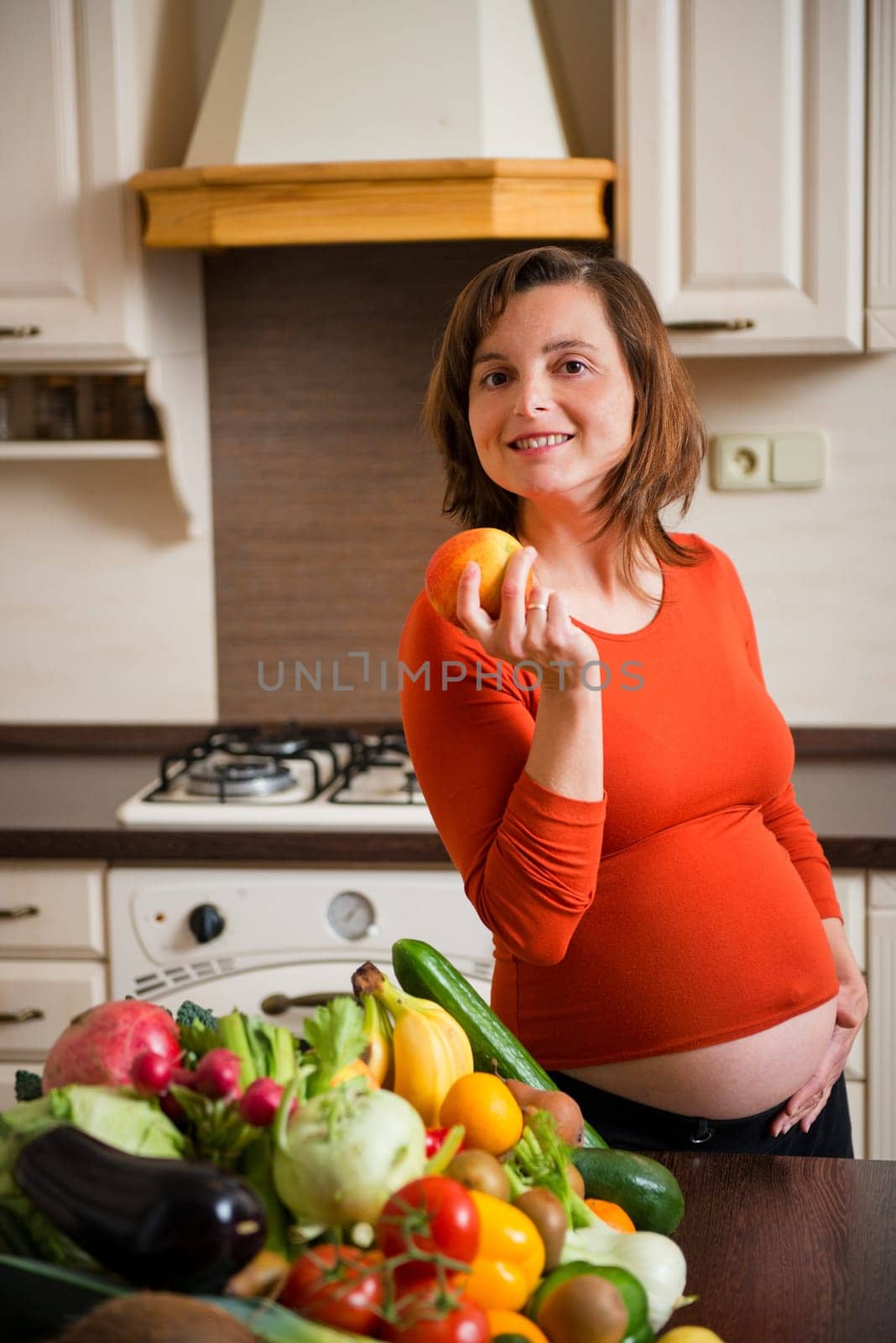 Pregnant woman with abundance of vegetables and fruits holding apple