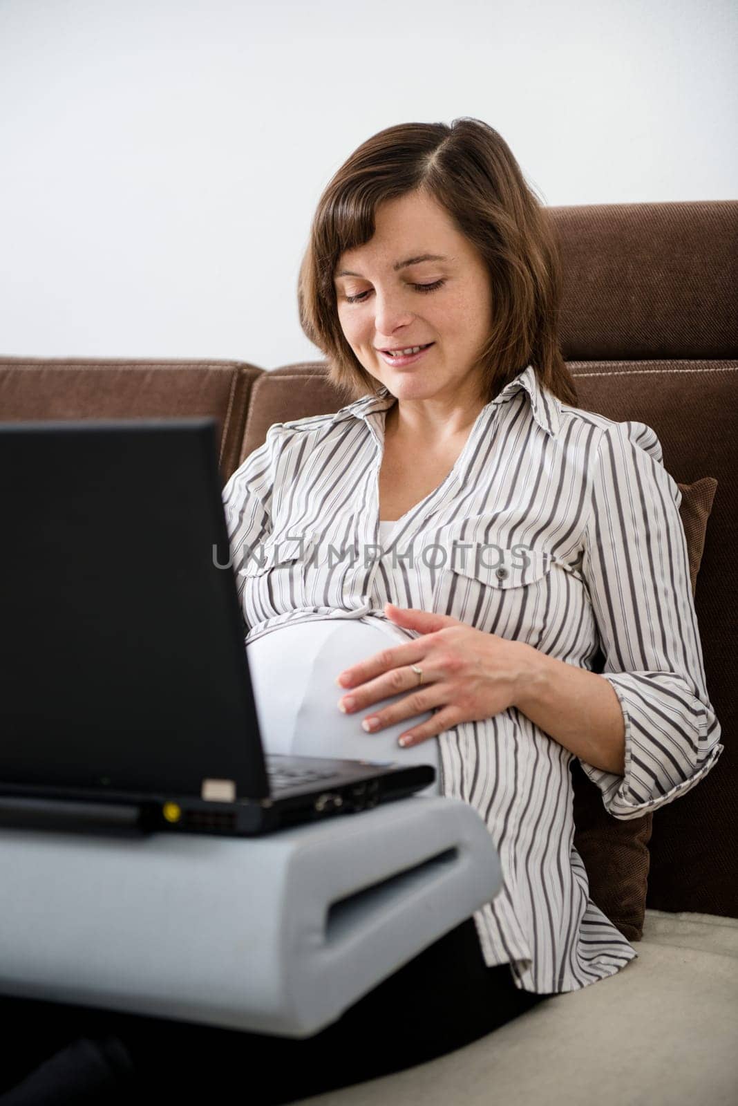 Pregnant woman working on laptop from home on sofa