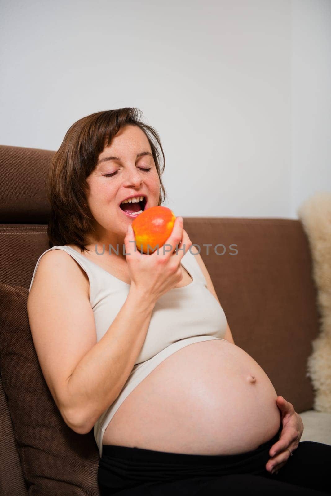 Lifestyle portrait of smiling pregnant woman eating apple at home