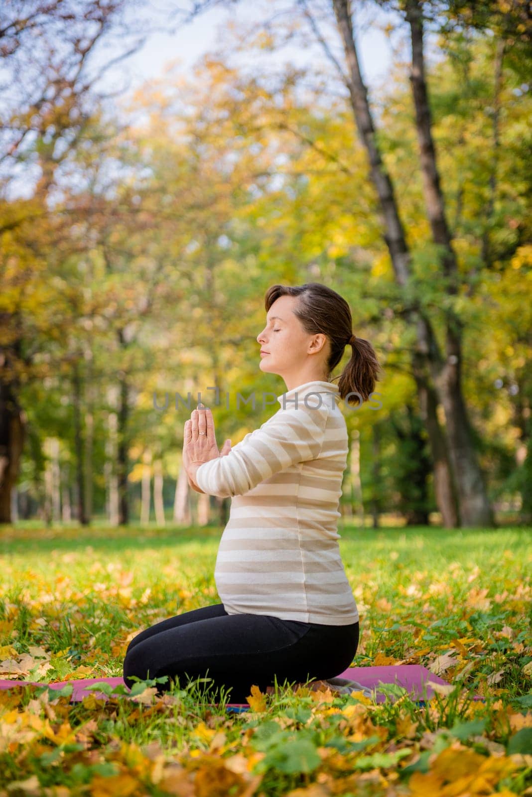 Young pregnant woman meditating outside in beautiful autumn nature