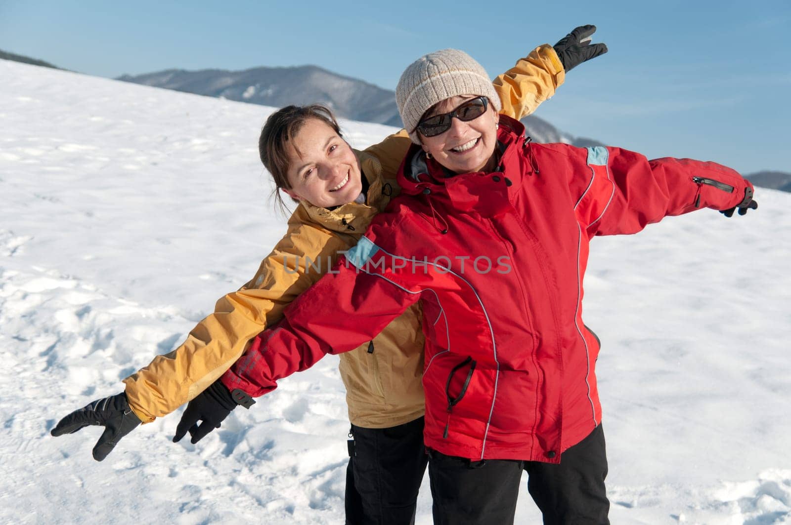 Winter lifestyle - happy smiling senior mother with her adult daughter in snow nature