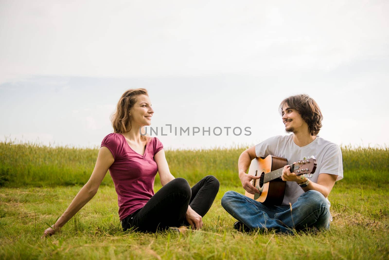 Young man playing guitar to his girlfriend in nature - dating couple