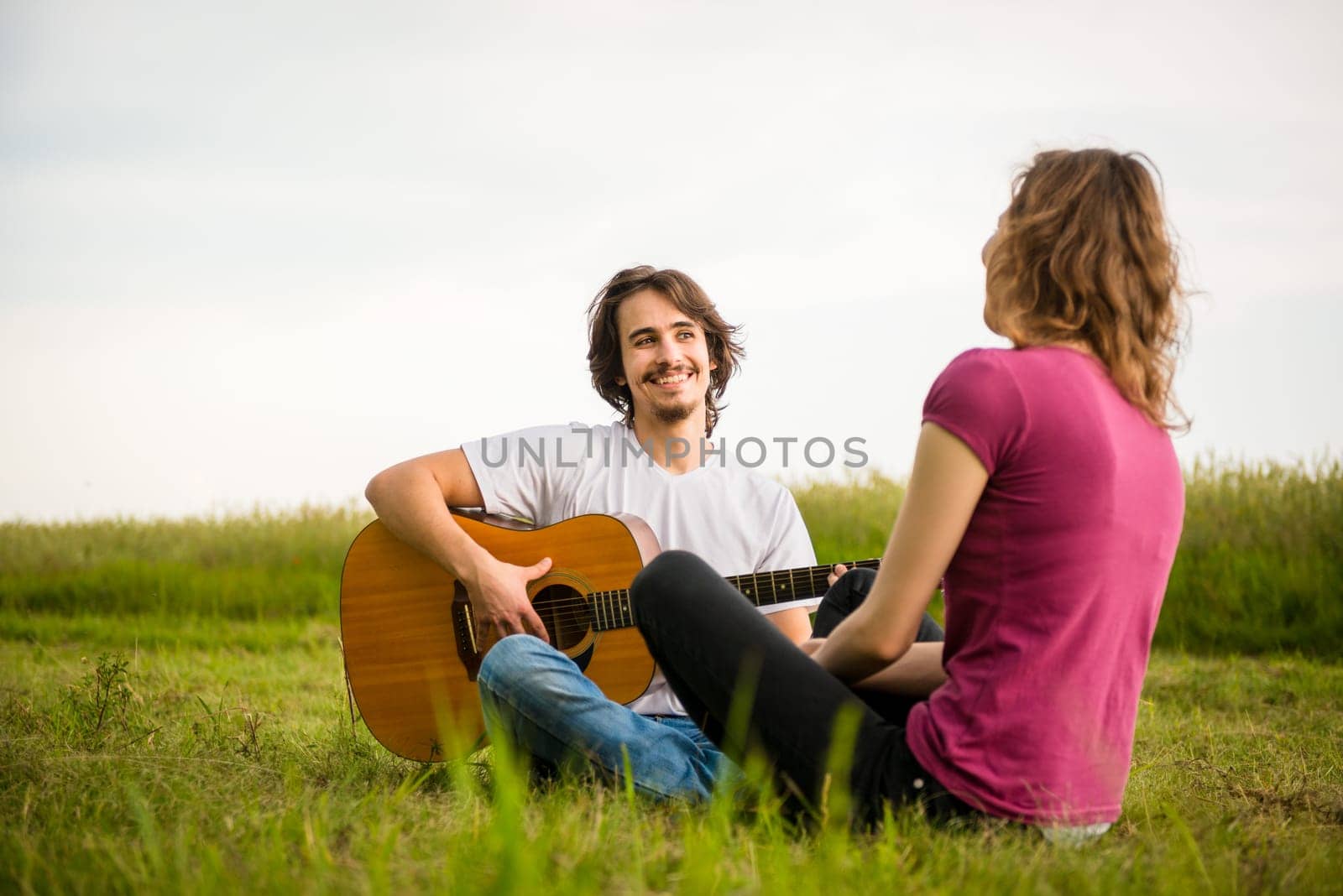 Young man playing guitar to his girlfriend in nature - dating couple