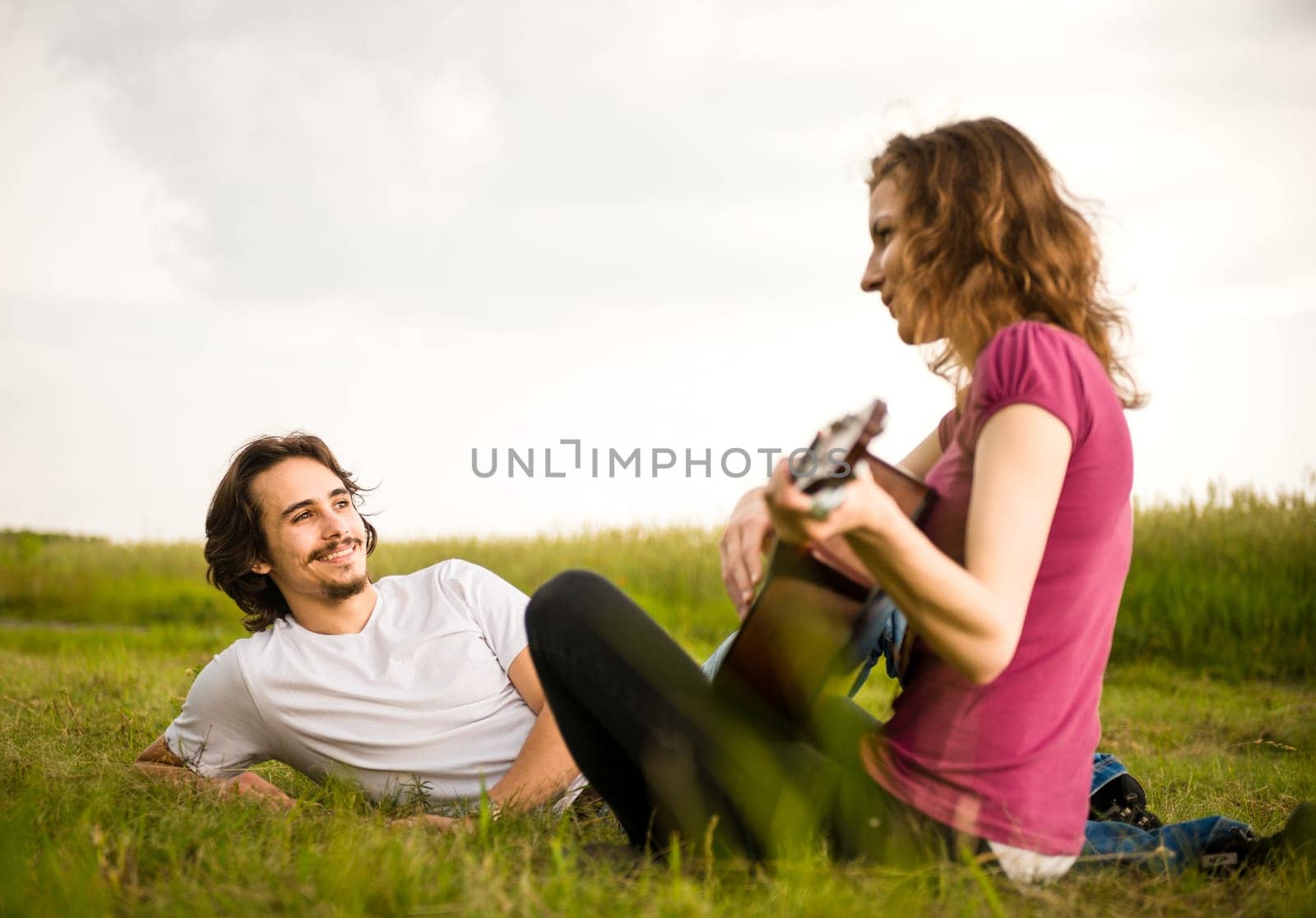 Young woman playing to his boyfriend on guitar - outside in nature