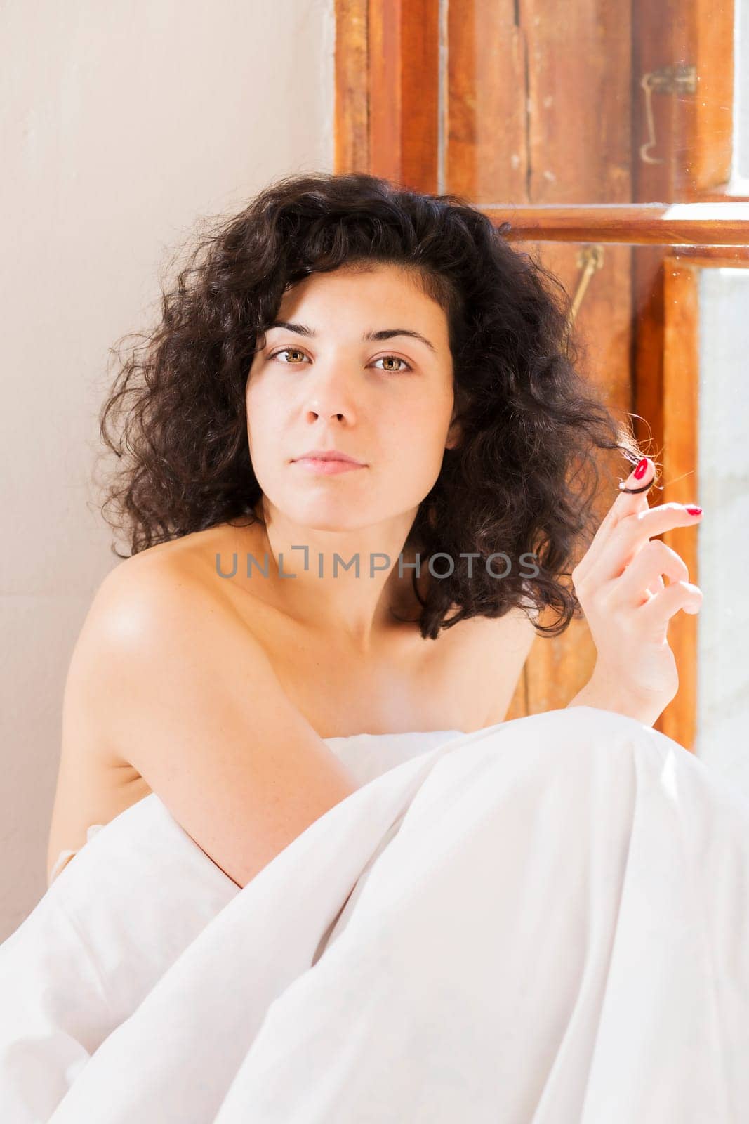 Pretty woman play with hair between white bedclothes