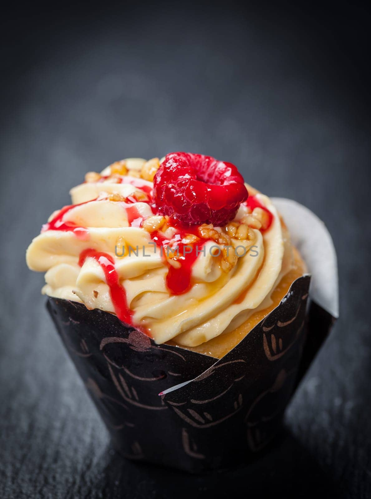 Delicious vanilla cupcake with raspberry on black background