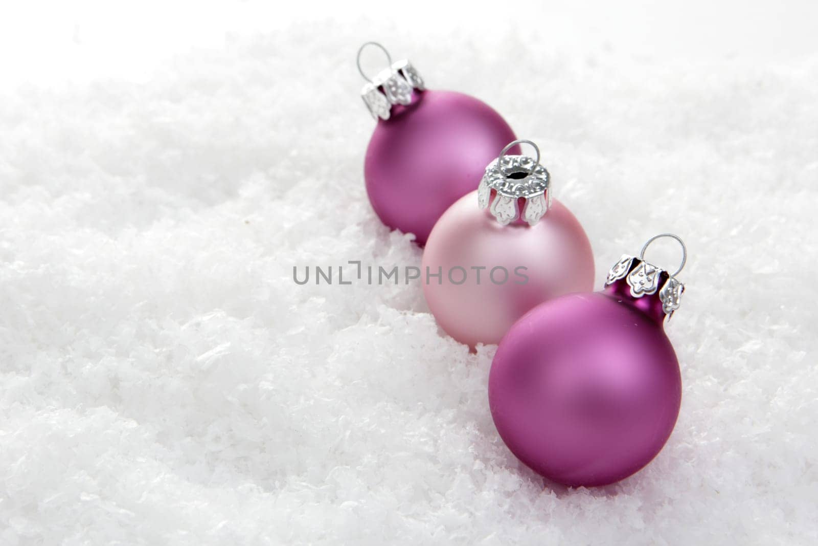 pink Christmas baubles on artificial snow with a white background