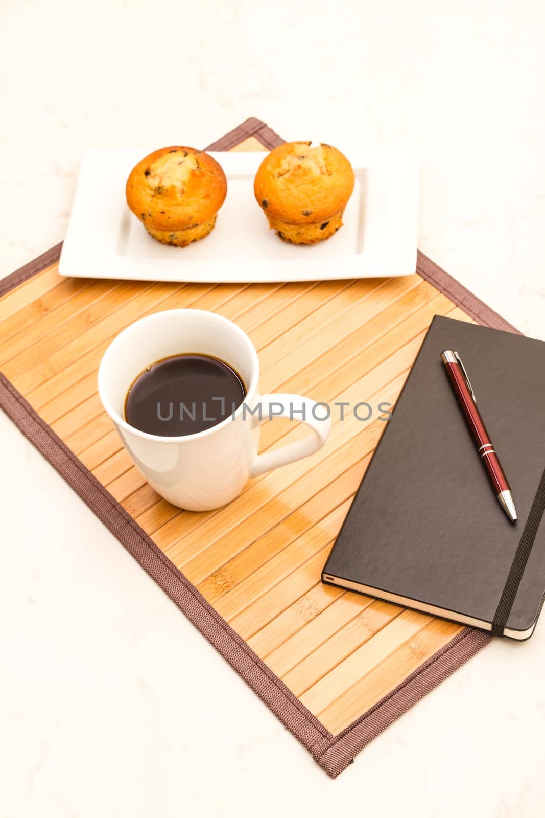Vanilla with chocolate chips Muffins on a white plate with  a cup of coffee meanwhile taking notes.