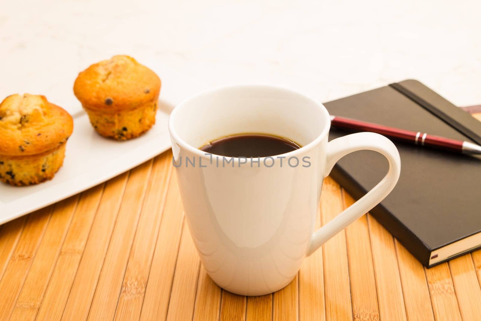 Vanilla with chocolate chips Muffins on a white plate with  a cup of coffee meanwhile taking notes.