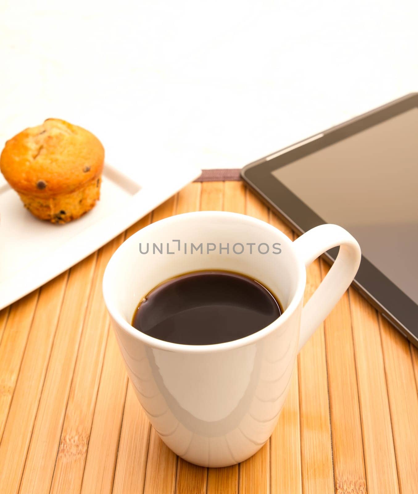 Vanilla with chocolate chips Muffins with  a cup of coffee meanwhile using the tablet..