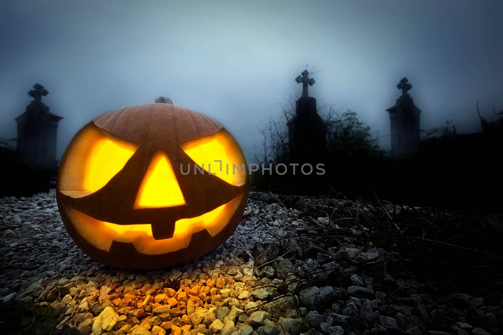 A glowing Jack O Lantern in a dark mist graveyard on Halloween