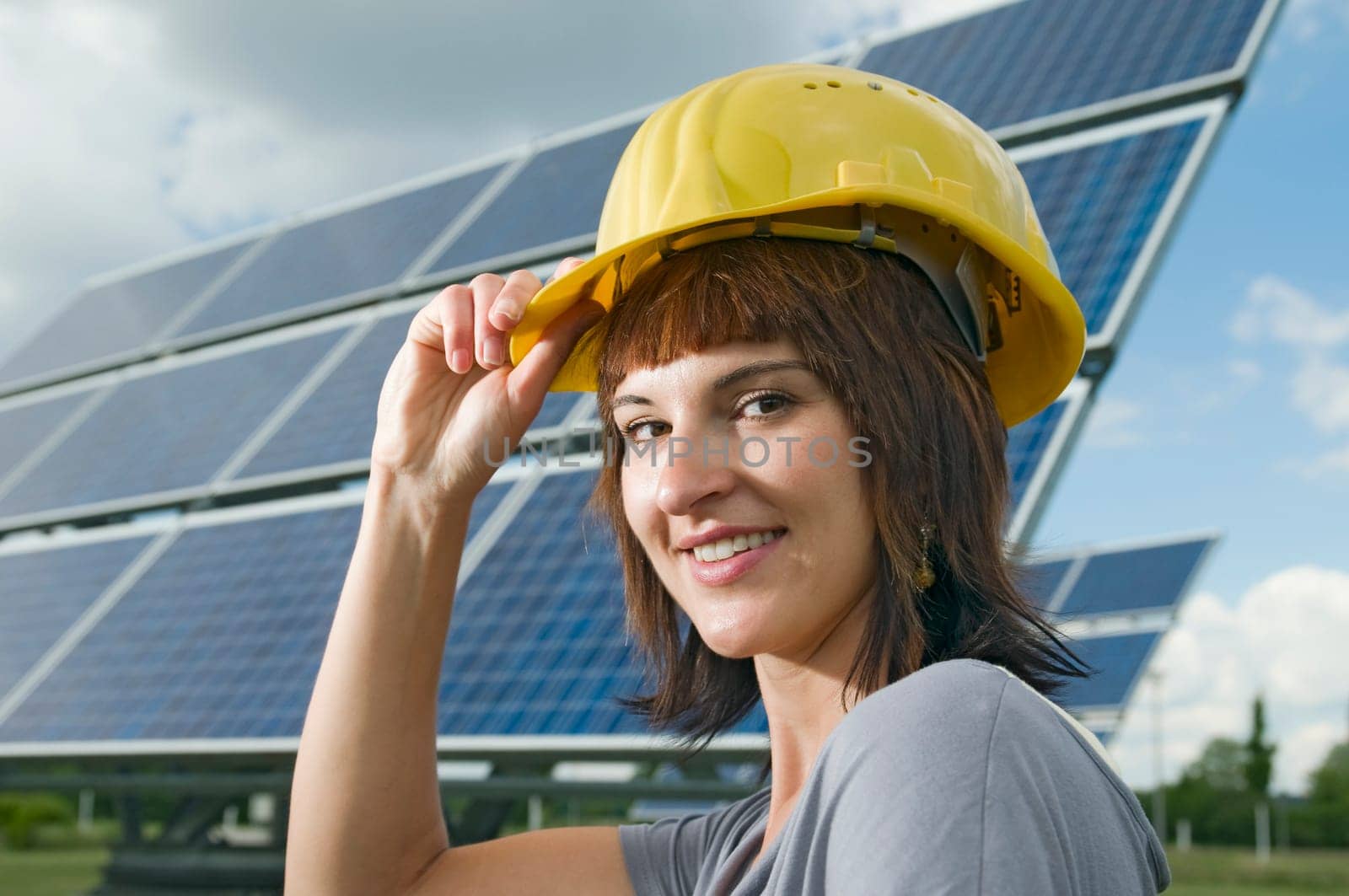 young brunette woman with yellow construction helmet in front of photovoltaic system