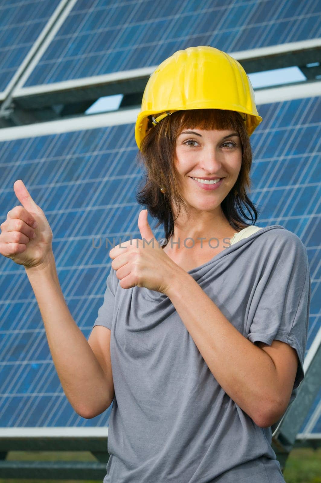 young brunette woman with yellow construction helmet in front of photovoltaic system