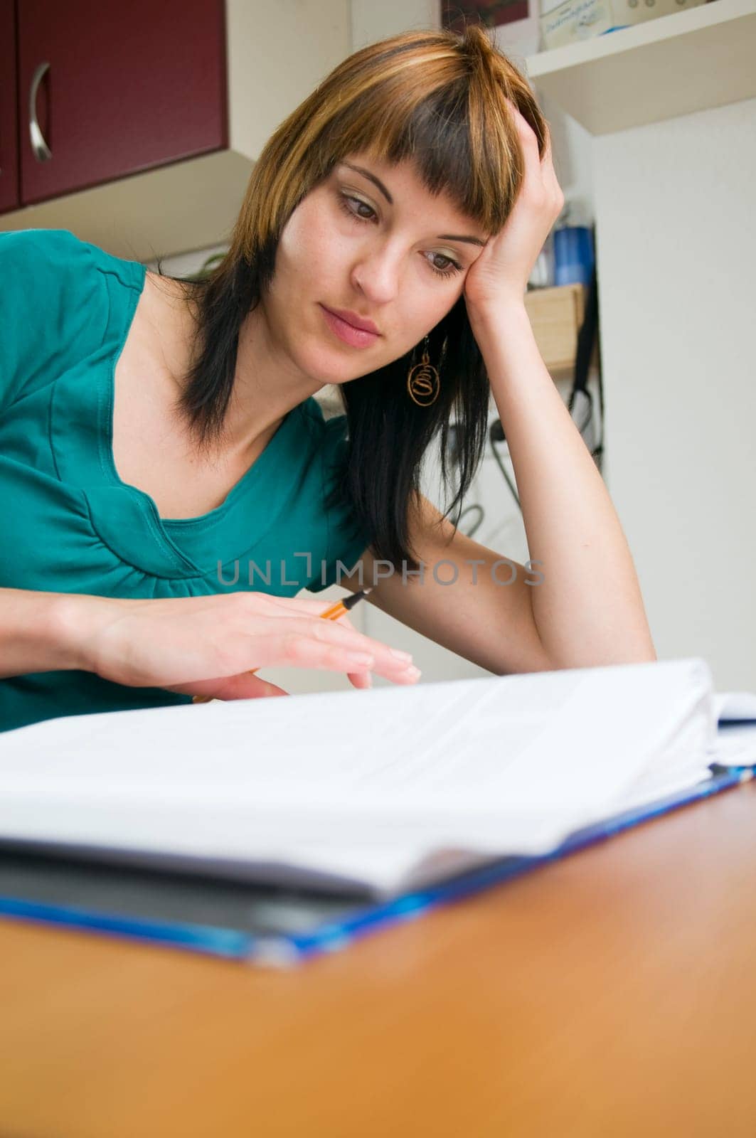 Head-and-shoulder view of a young,brunette woman sitting at the table with pen in hand and binder in front of her