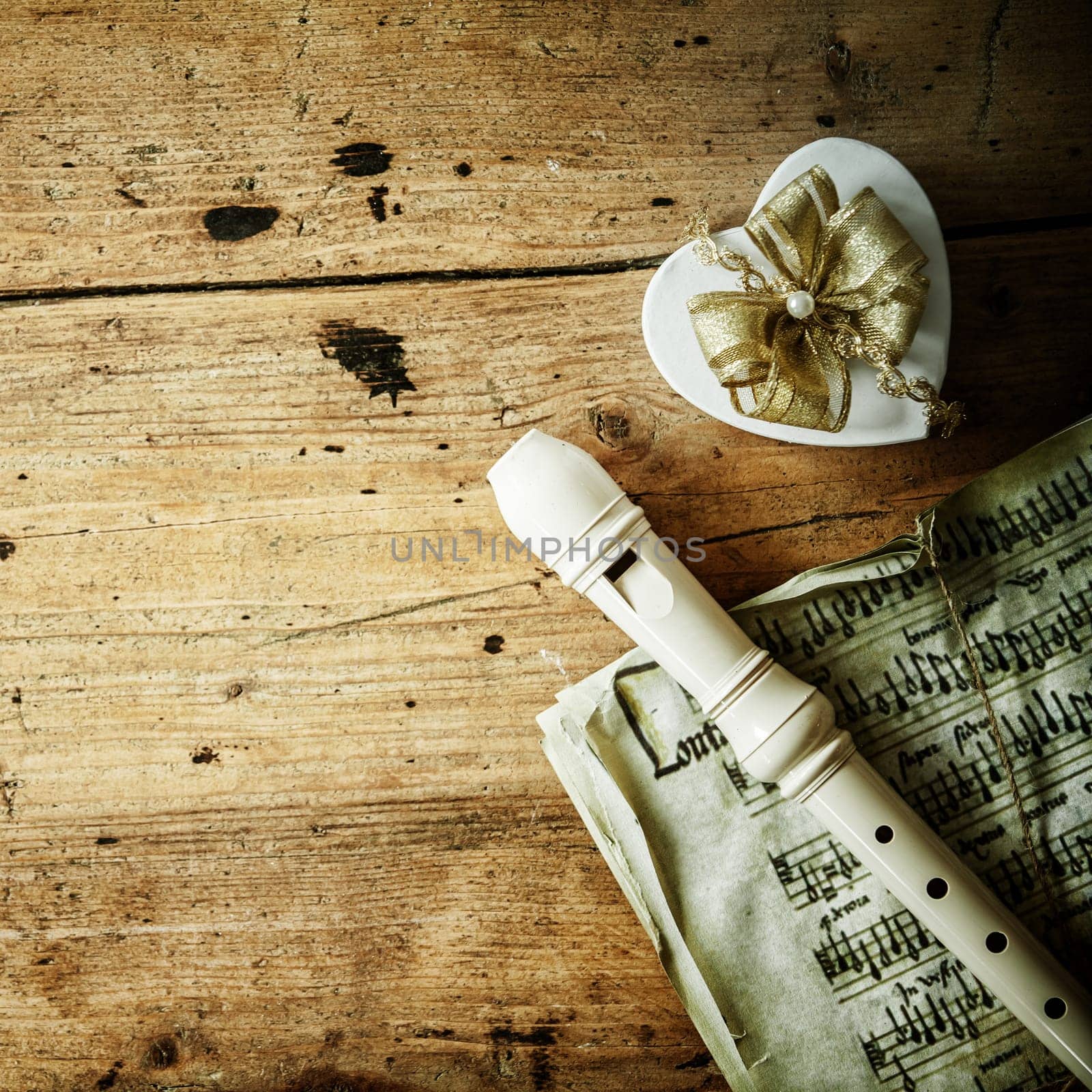 Conceptual image of Christmas night music with a recorder of flute lying on an old music score alongside a decorative heart shaped gift with an ornamental bow, copyspace on the rustic wood background