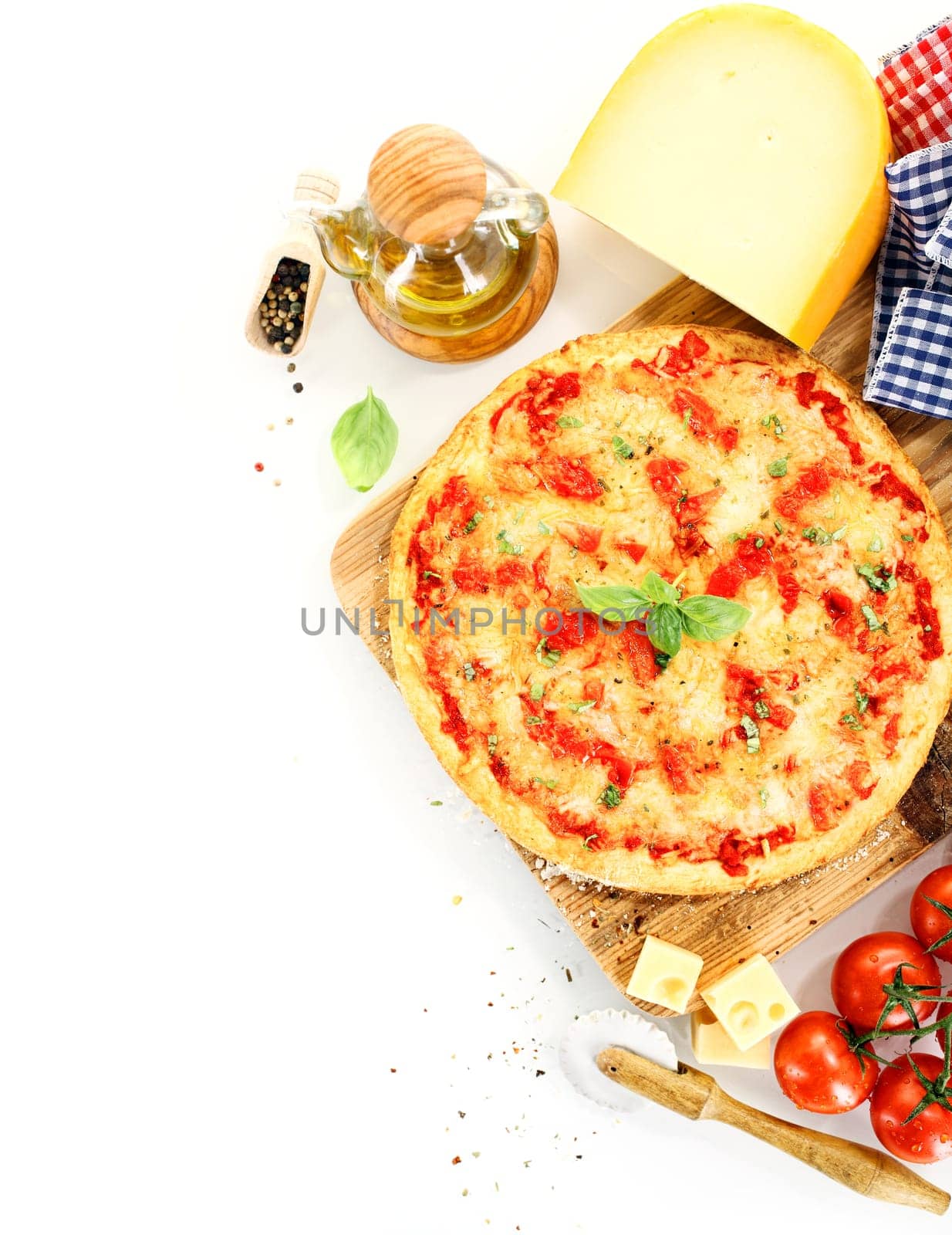 Top view of a pizza Margherita surrounded by ingredients like tomato, cheese, basil, olive oil and pepper and kitchen tools