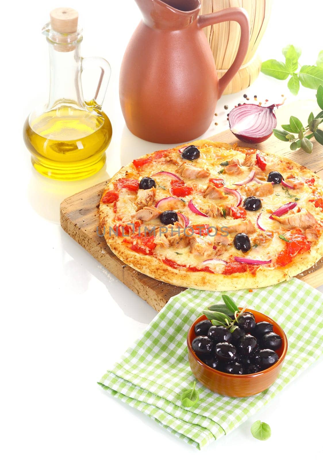 Pizza made of tuna, olives, onion and basil over a wooden board surrounded by the ingredients