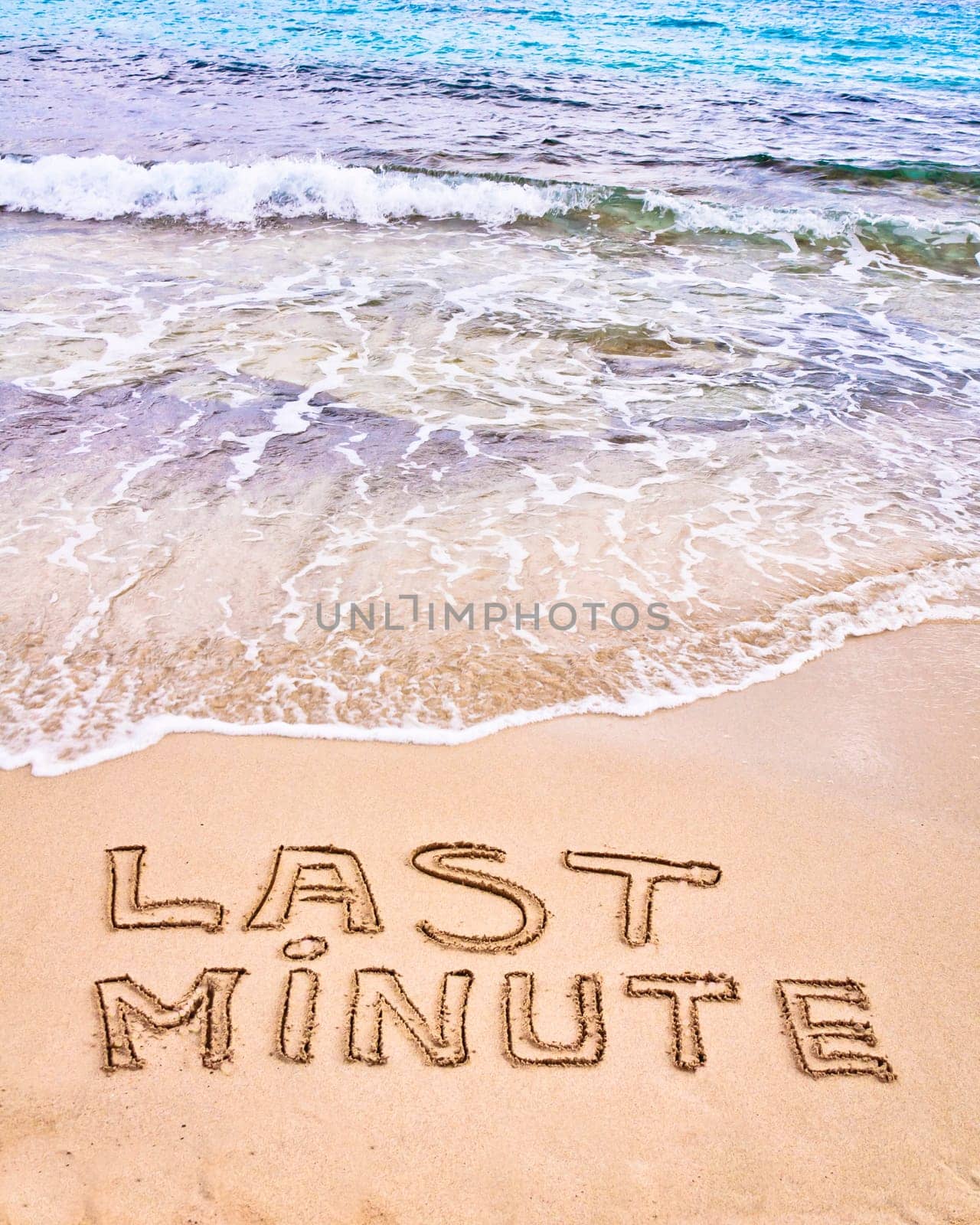 Last Minute written on sand, with waves in background, vacation concept