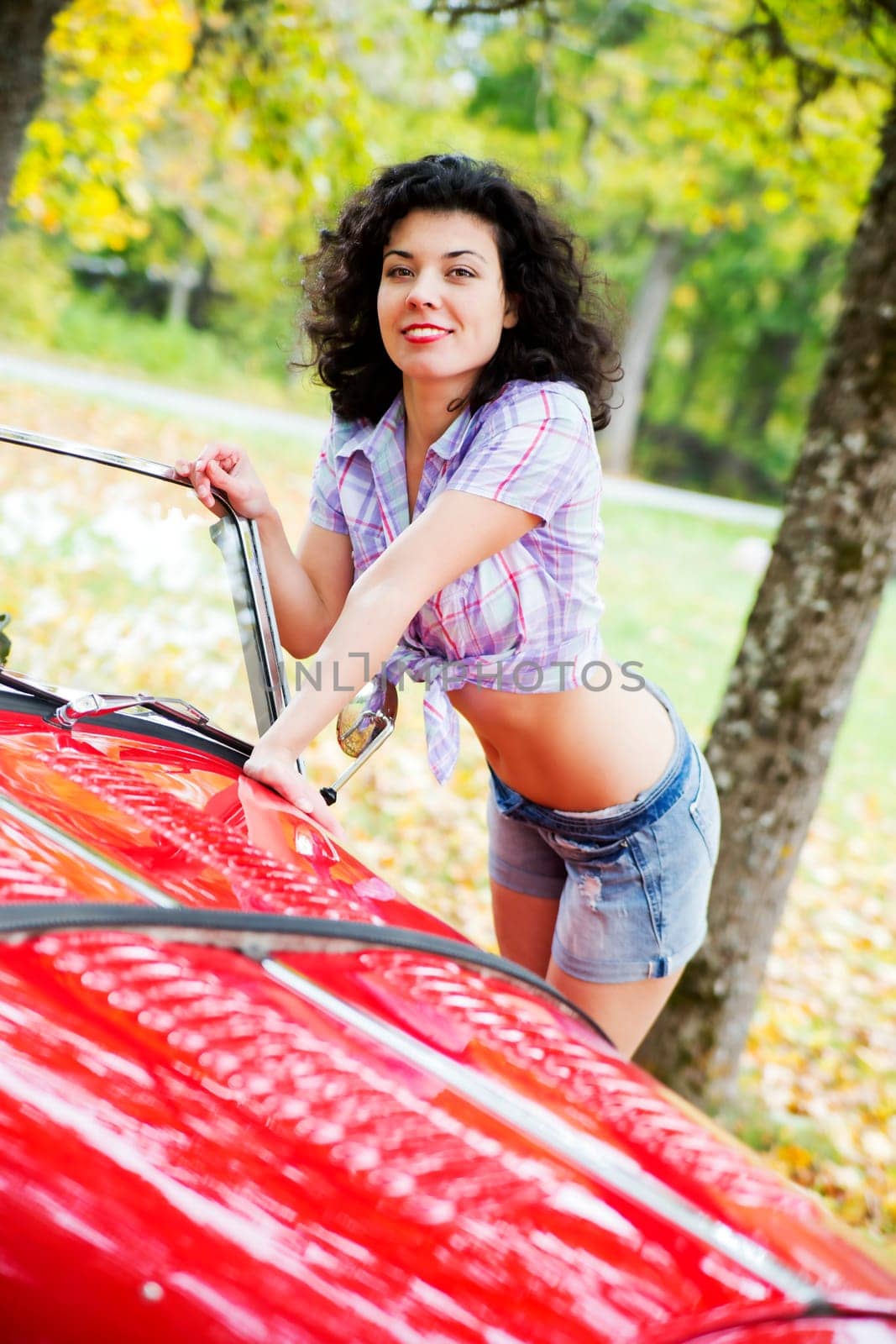Woman in shirt posing on red car side