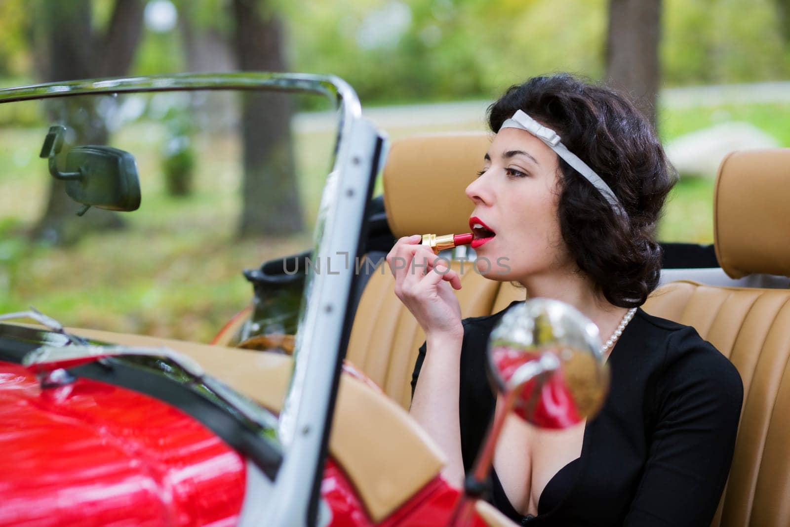 Zoomed woman stains the lips before car mirror