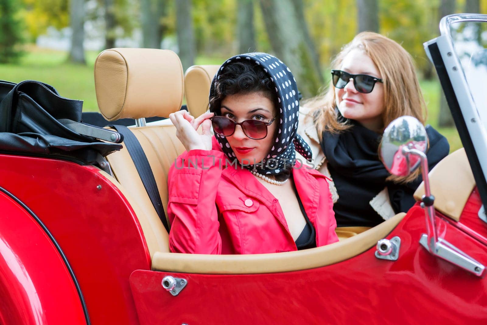 Fashionable women at retro red car look satisfied