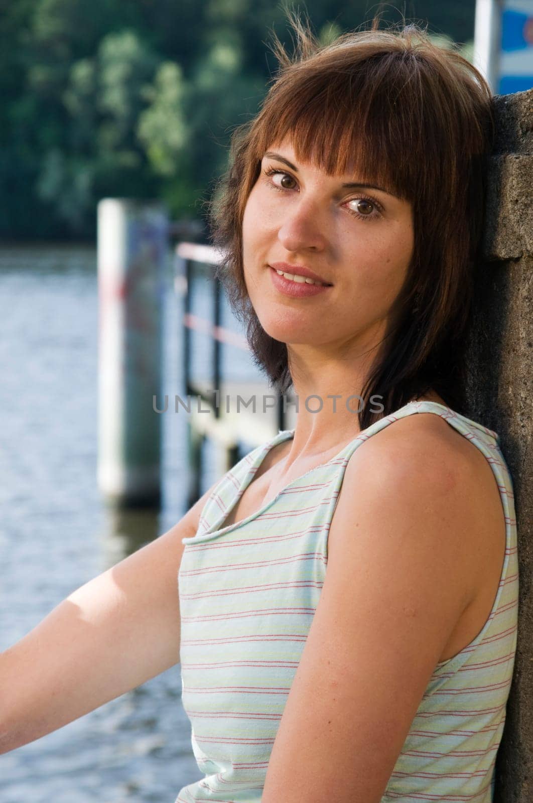 Side view Head-and-shoulder portrait of a young,brunette woman in a sleeveless top at the lake with a view into the camera