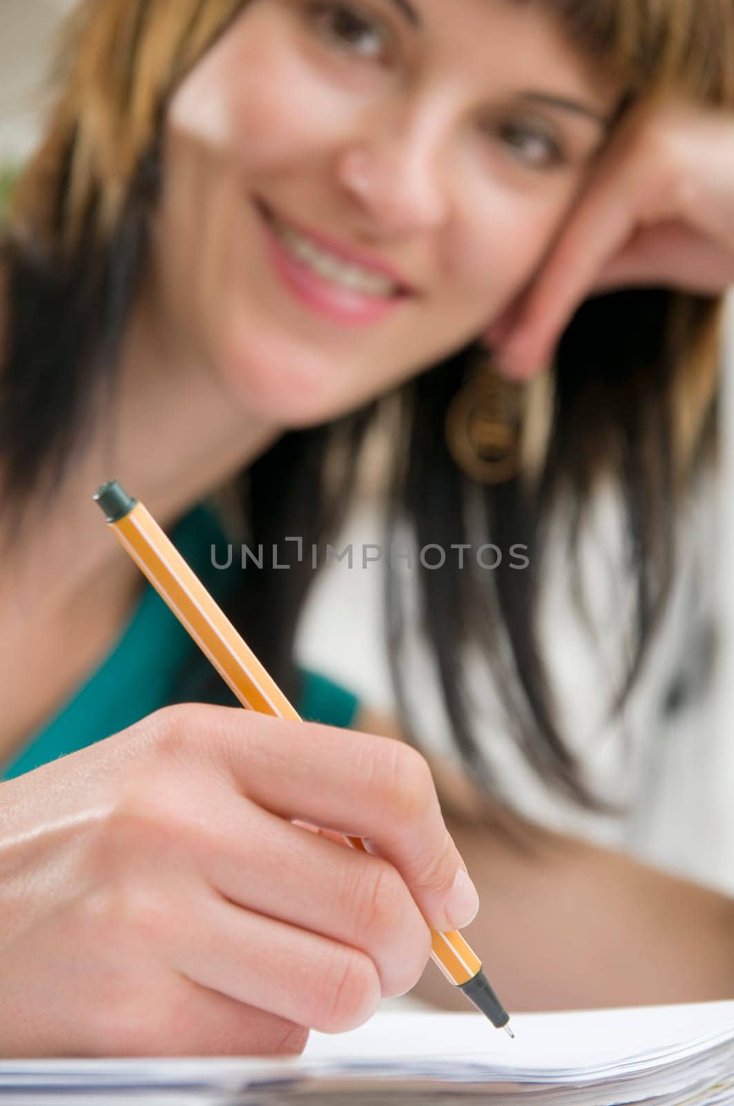 Head-and-shoulder view of a young,brunette woman sitting at the table with pen in hand and binder in front of her