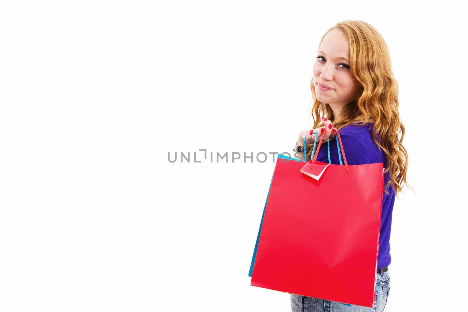 Young red-haired woman with shopping bags turns around against a white background