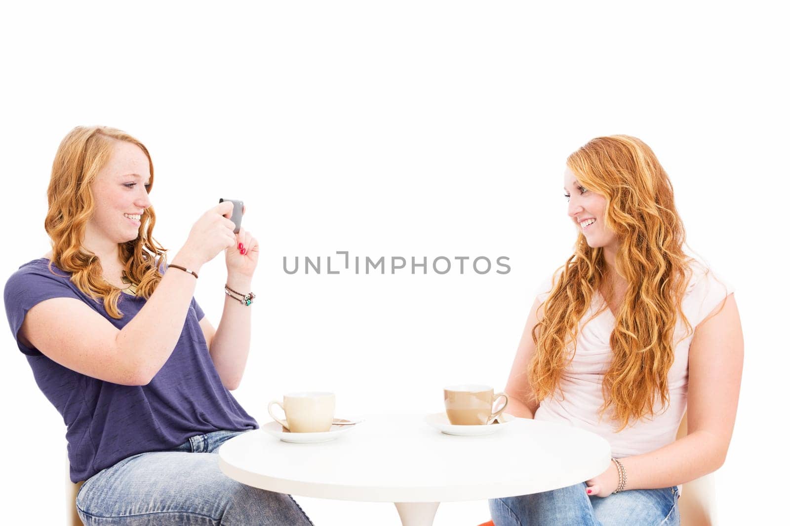 Young woman takes a photo of her friend in front of a white background