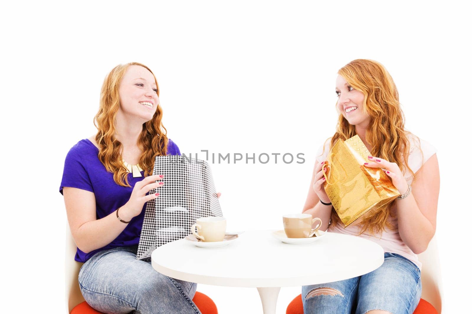 Two happy women having coffee with shopping bags against a white background
