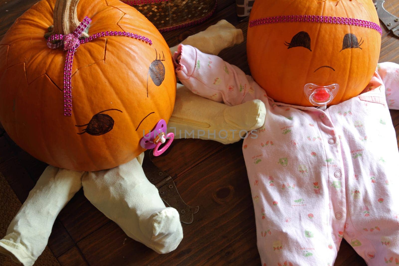 Two pumpkins dressed up as princess babies with pacifiers, seen from above.