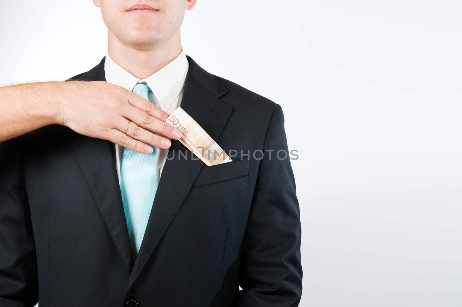 Upper body view without head of a young man in a black suit against a white background  a hand protruding into the picture from the left inserts a folded banknote into the outer breast pocket