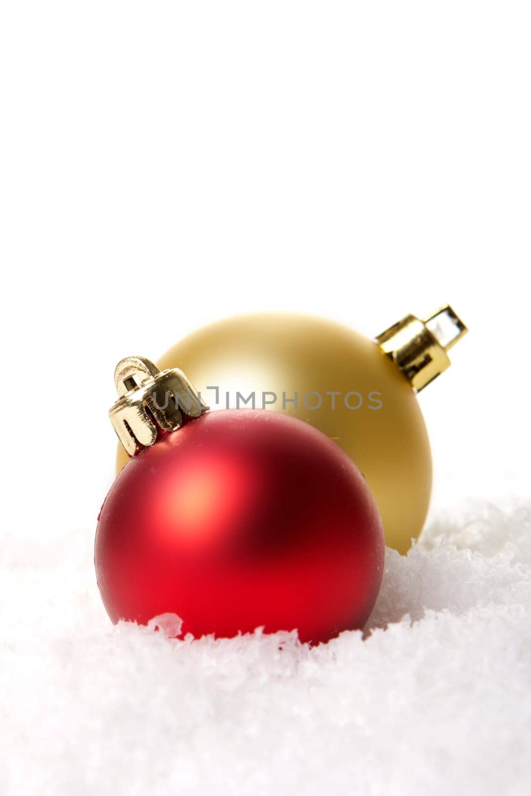 golden and red Christmas baubles on artificial snow with a white background