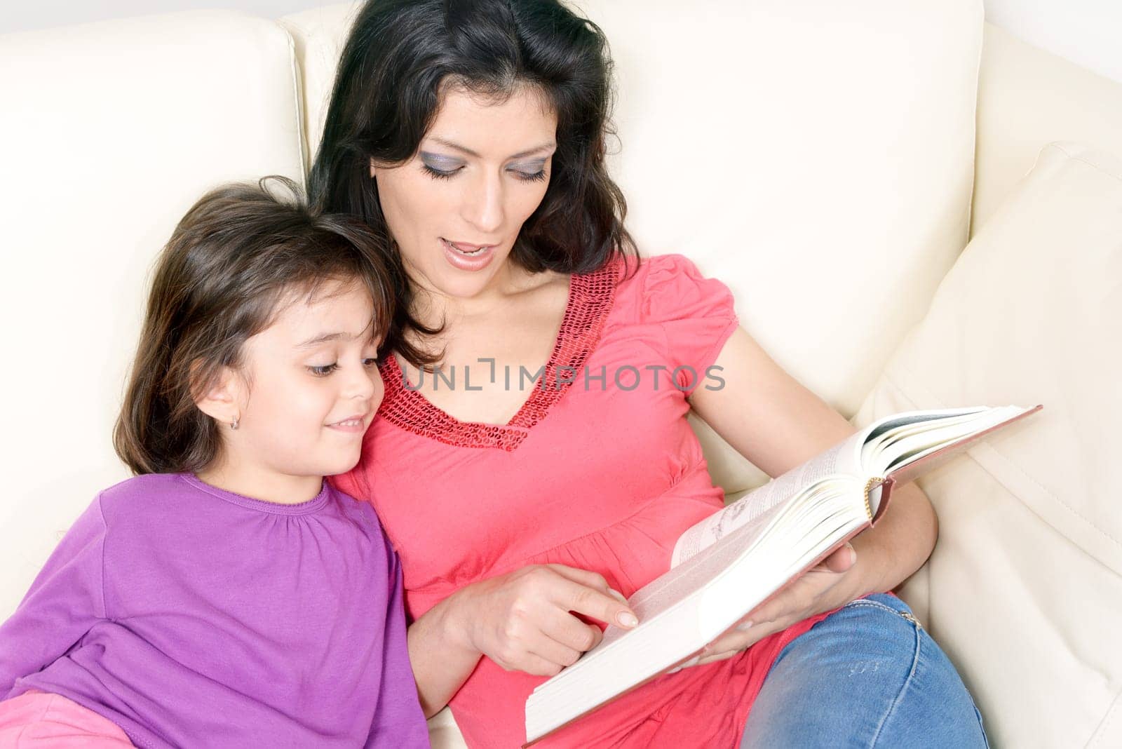 Mother and daughter reading a book together, comfortably seated on the sofa. Concept of family.