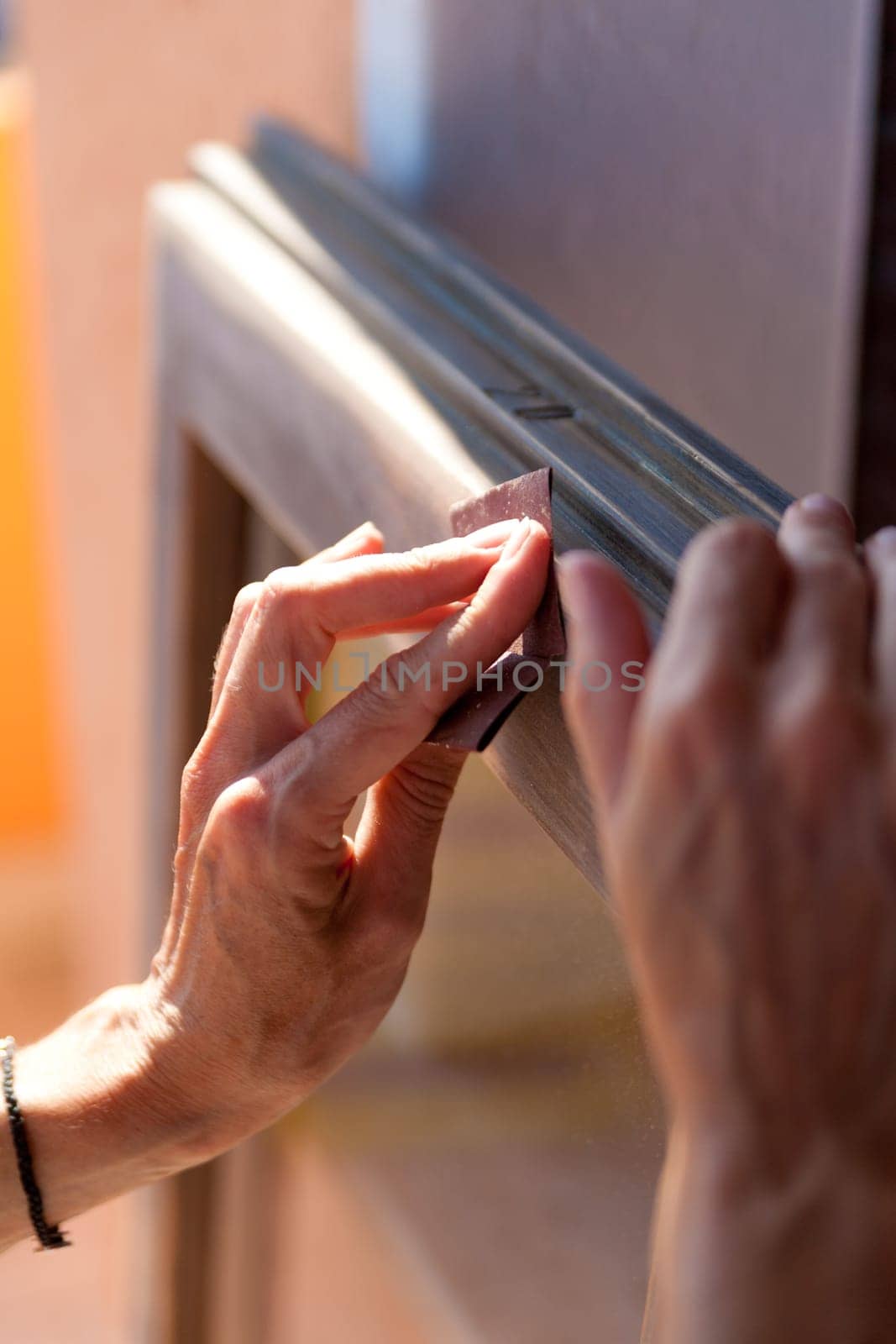 Hands of a woman with sandpaper doing DIY work on wooden fixtures