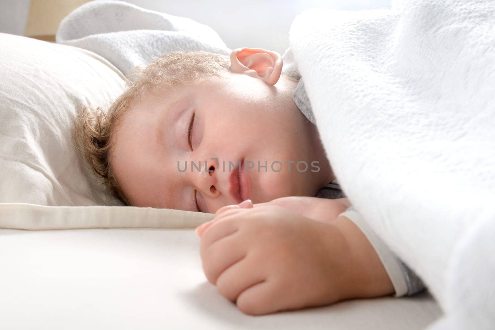little blond boy, relaxed sleeping on her bed wrapped in a soft blanket