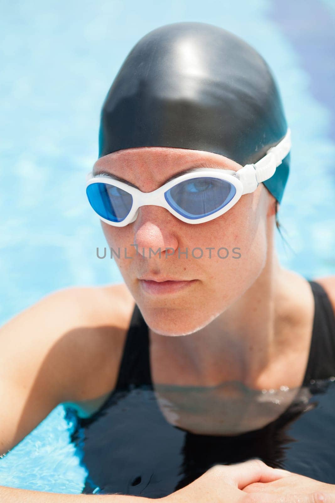 Female swimmer resting at edge swimming pool concetrating and peering through goggles