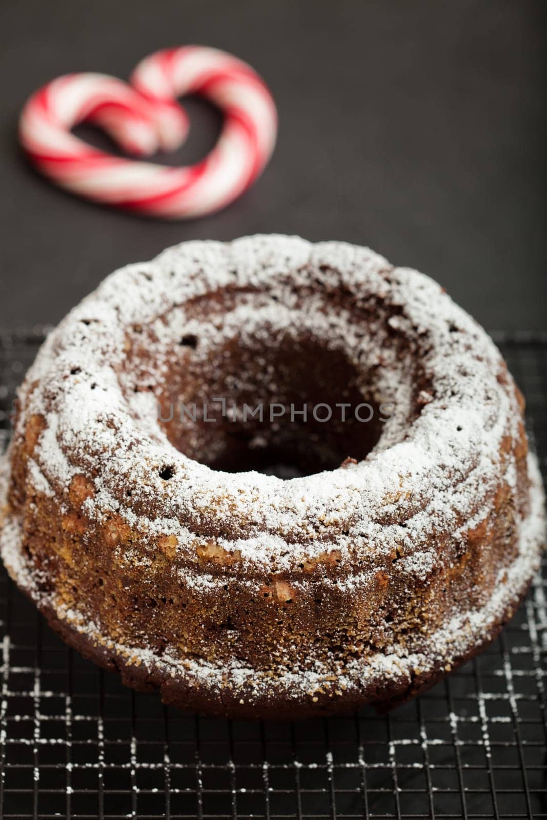 Closeup of dry chocolate cake sprinkled with icing sugar and resting on metal grill with candy heart with red swirls in background