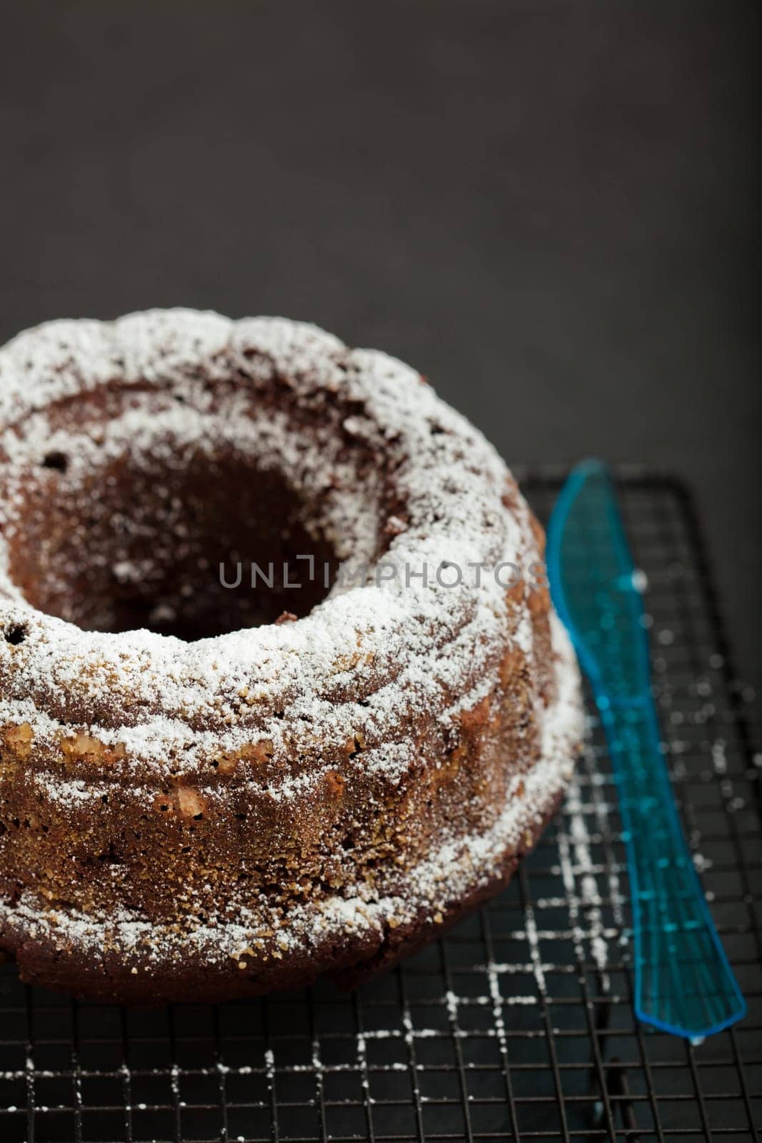 Dry chocolate cake sprinkled with icing sugar and blue plastic fork resting on metal grill