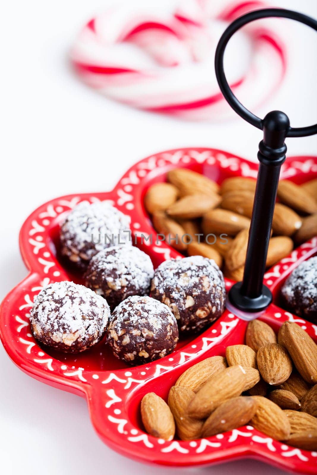 Closeup of tray of almonds and chocolate balls and hard handy heart with red swirls in background on light background