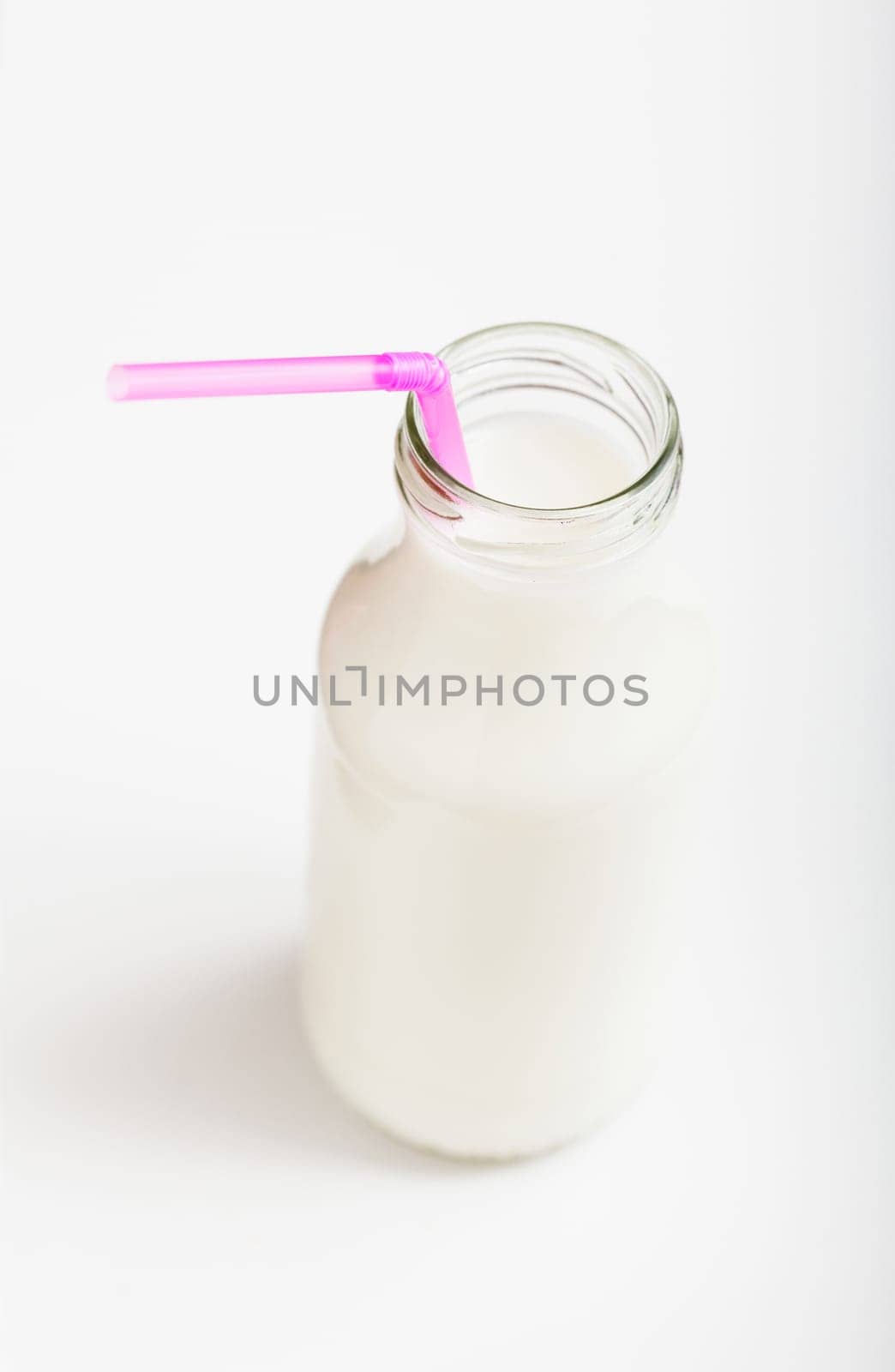 Closeup of fresh milk in glass jar with pink straw on light background