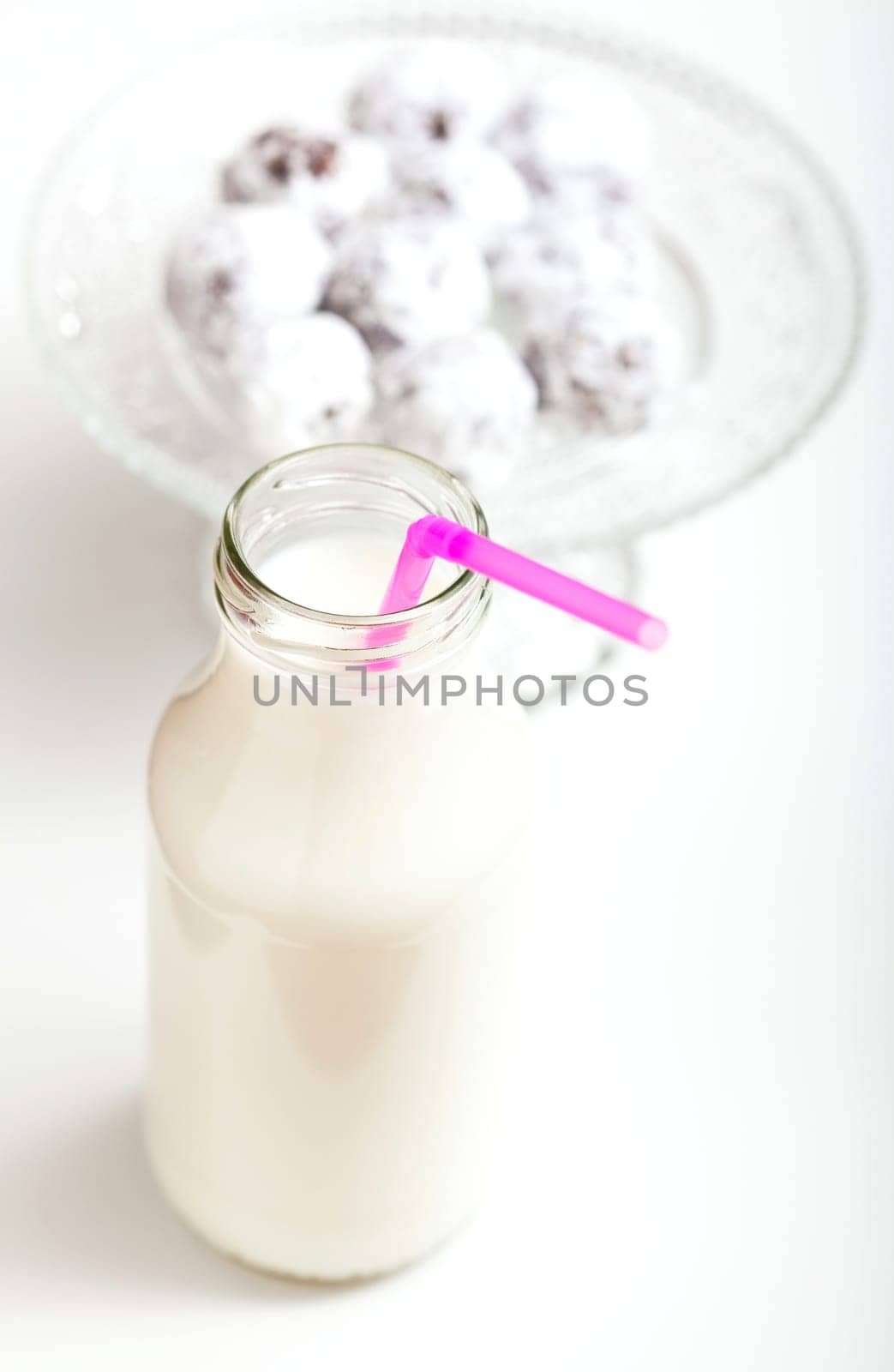 Closeup of milk in glass jar with pink straw with glass serving tray of chocolate balls sprinkled with icing sugar in background