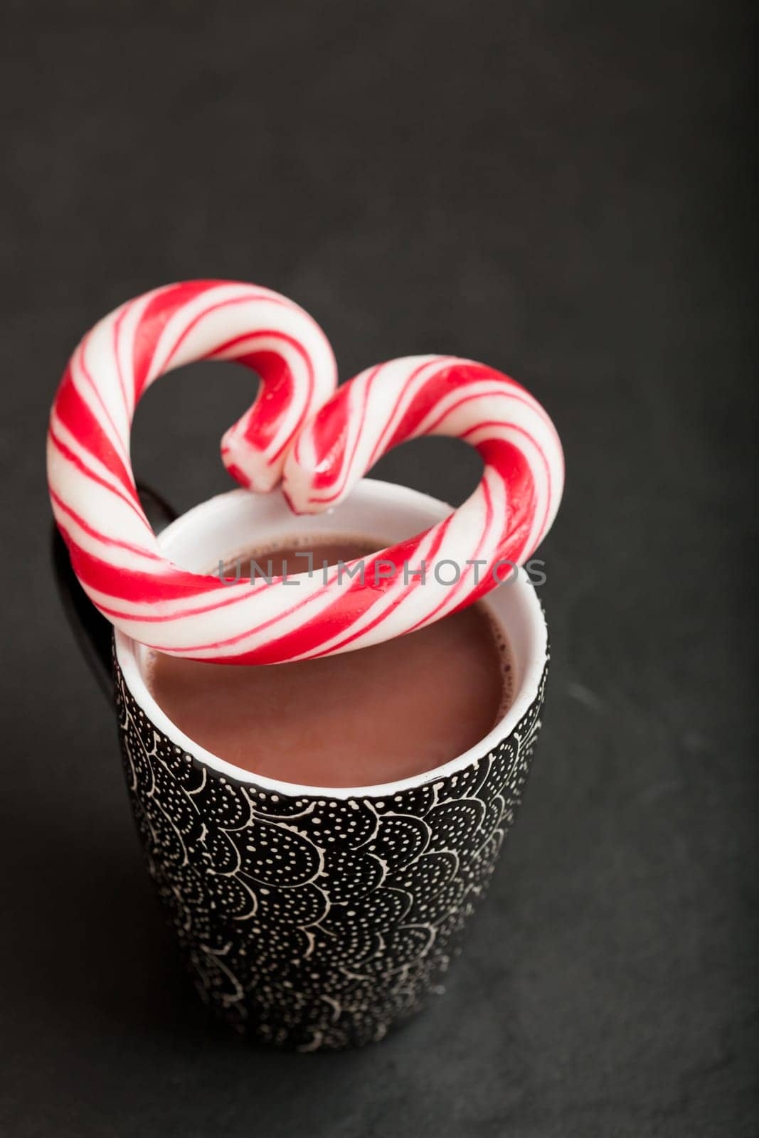 Closeup of mug of hot chocolate with hard candy heart with red swirls resting on top
