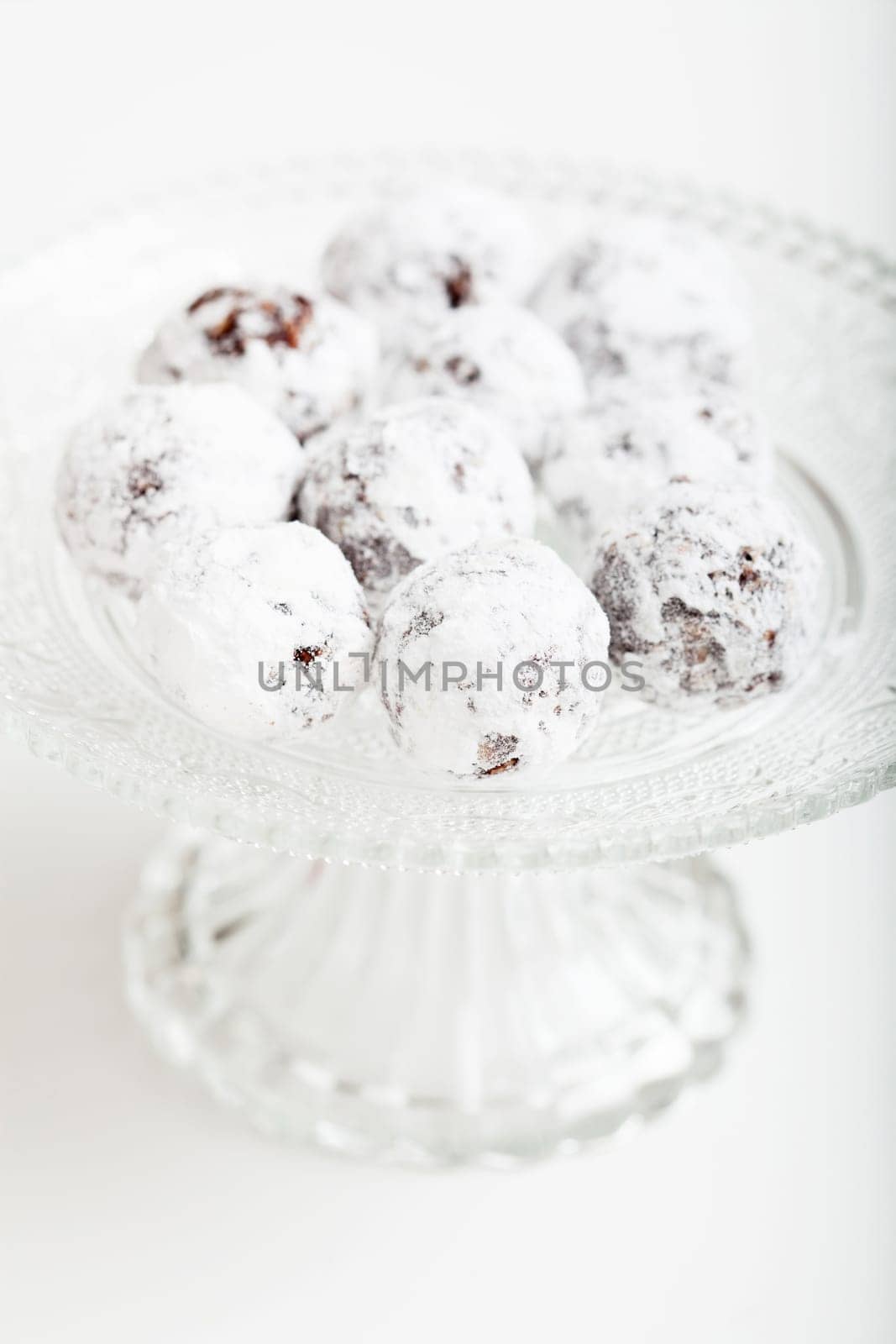 Closeup of chocolate balls sprinkled with icing sugar on glass serving tray on light surface