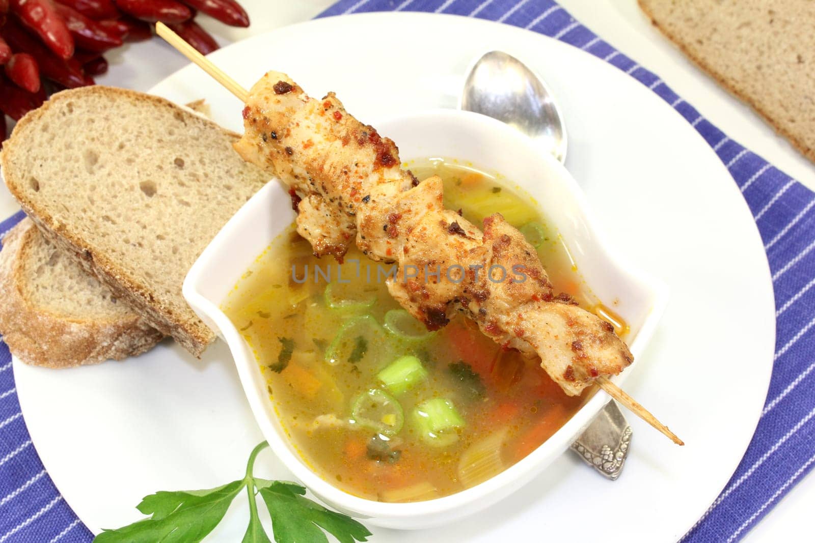 a bowl with poultry consommé and a chicken skewer